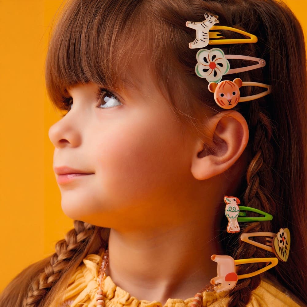 Child with colorful hair clips in braided hair against an orange background