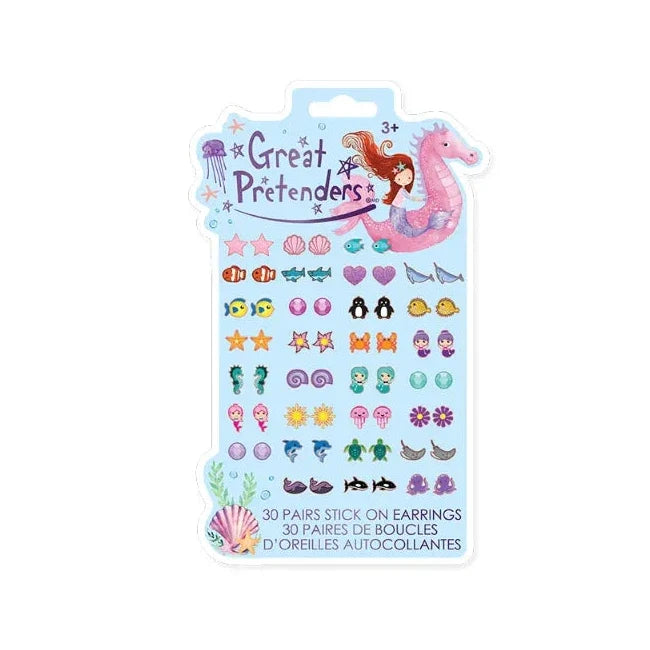 A package of 'Great Pretend' mermaid-themed stick-on earrings on a white background. The light blue card features cartoon illustrations of a mermaid, a pink seahorse, a jellyfish, and an octopus, with rows of colorful, animal-shaped earrings including fish, sharks, penguins, dolphins, and seashells.