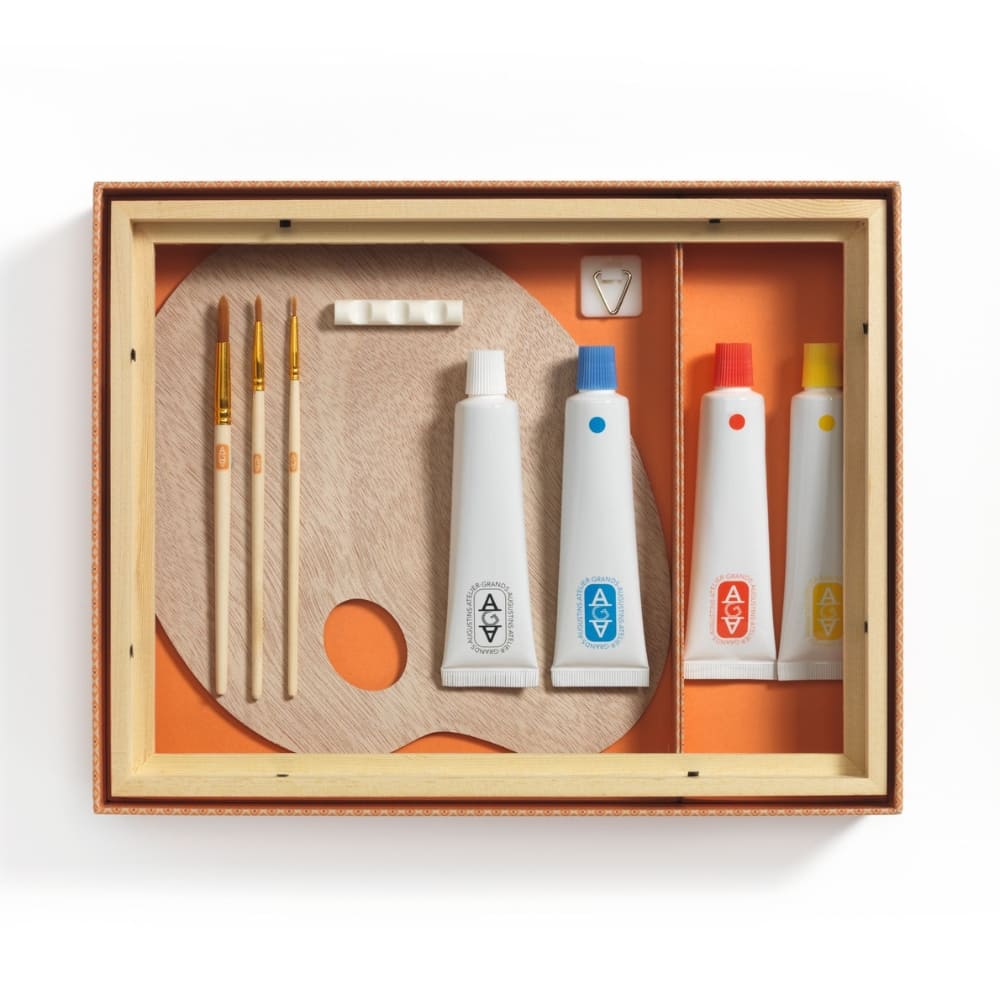 Set of art supplies including paintbrushes and tubes in a wooden box on a white background