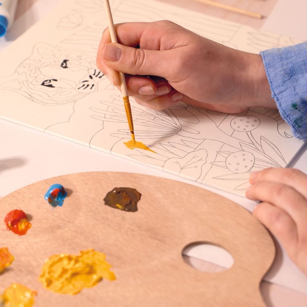 Person painting on a coloring book with a paintbrush and palette