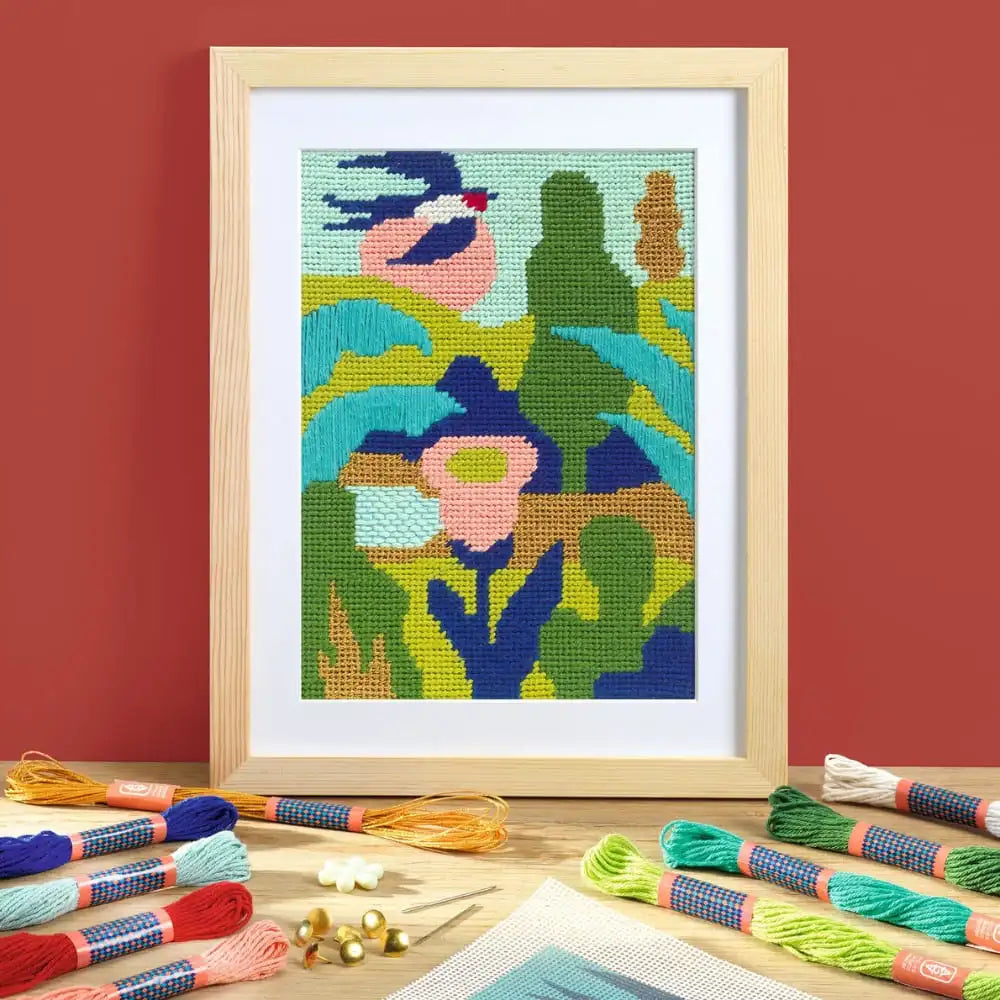 Framed cross-stitched artwork with colorful floral design on a red wall, surrounded by embroidery threads.