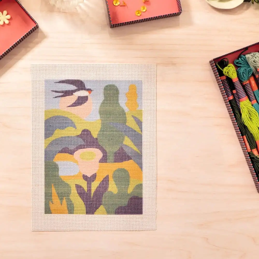 Cross-stitch pattern on a wooden surface with fabric and threads nearby