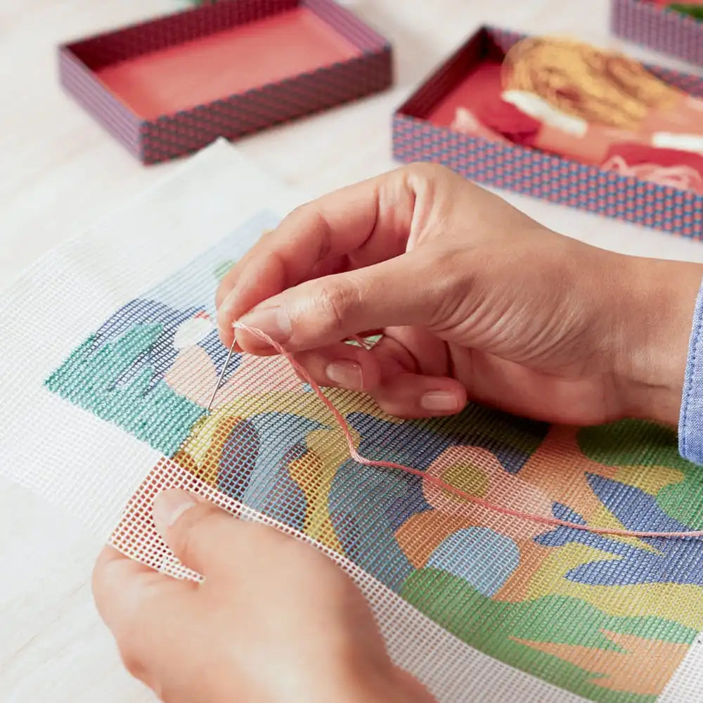 Hands working on a cross-stitch project with colorful fabric and threads.