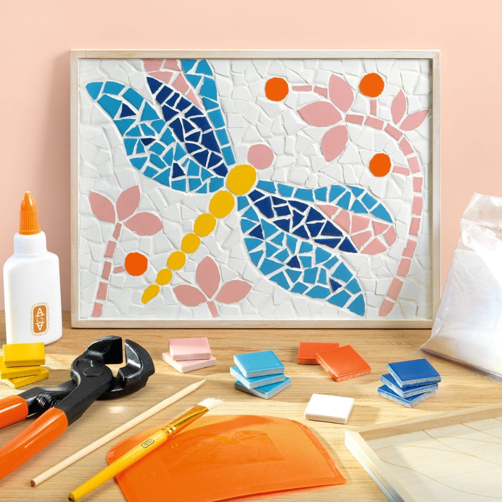 Mosaic artwork of a dragonfly on a wooden surface with tools and materials.