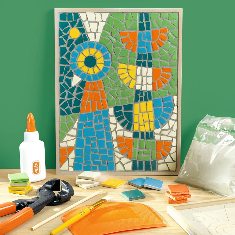 Colorful mosaic art piece on a wooden board with tools and materials on a green background