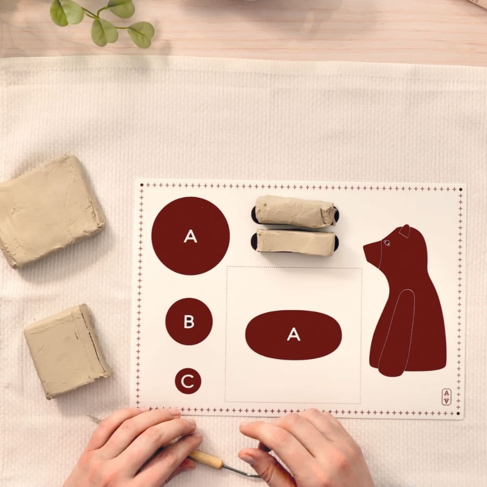 Hands working with clay and a template on a white surface