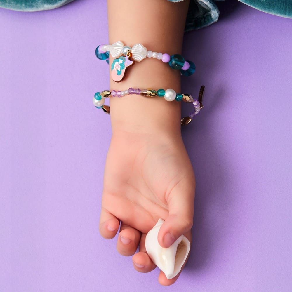 Child's hand wearing two beaded bracelets on a purple background