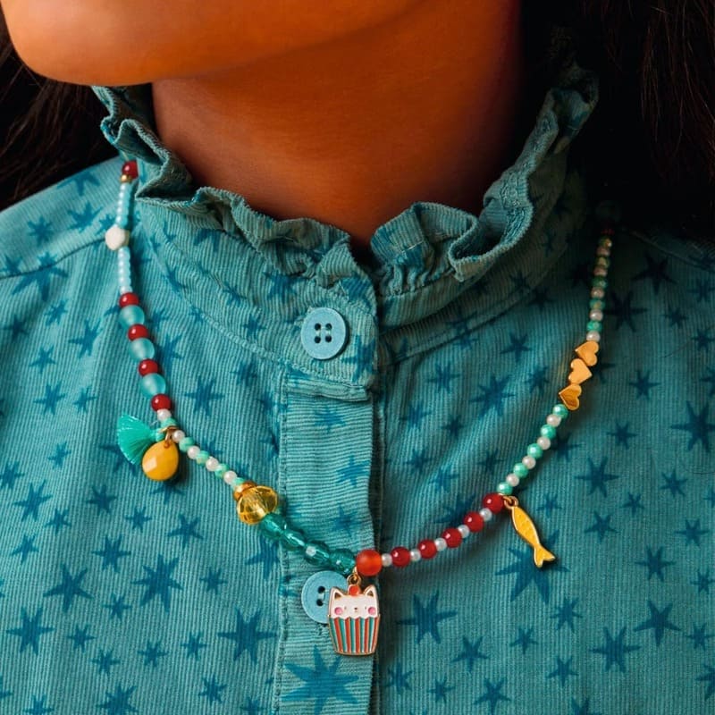 Close-up of a colorful beaded necklace with charms on a person wearing a blue patterned shirt.
