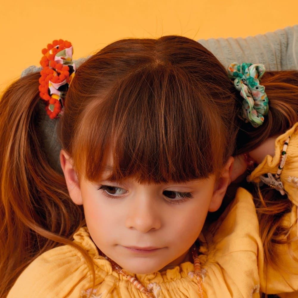 Young girl with pigtails wearing a yellow top against an orange background