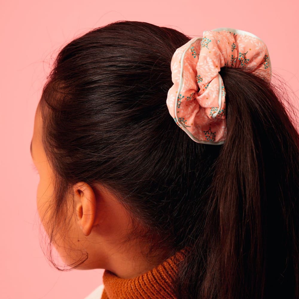 Person with a pink scrunchie in their hair against a pink background