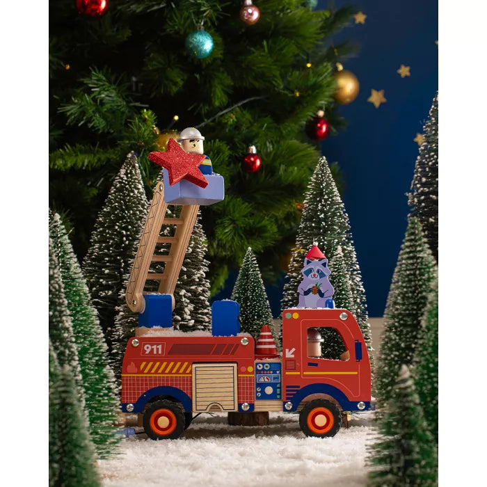 Toy fire truck with a ladder and star-shaped block in front of a decorated Christmas tree.