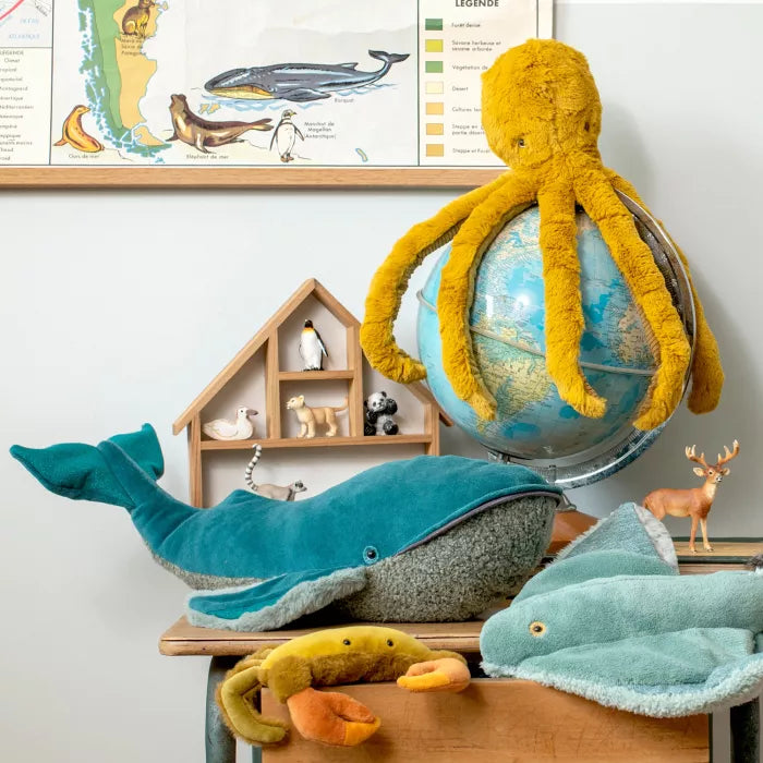 Plush toy octopus on a globe with whale and deer toys below, against a white wall with a framed chart.
