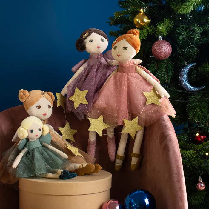 Three dolls with star decorations on a chair next to a decorated Christmas tree.