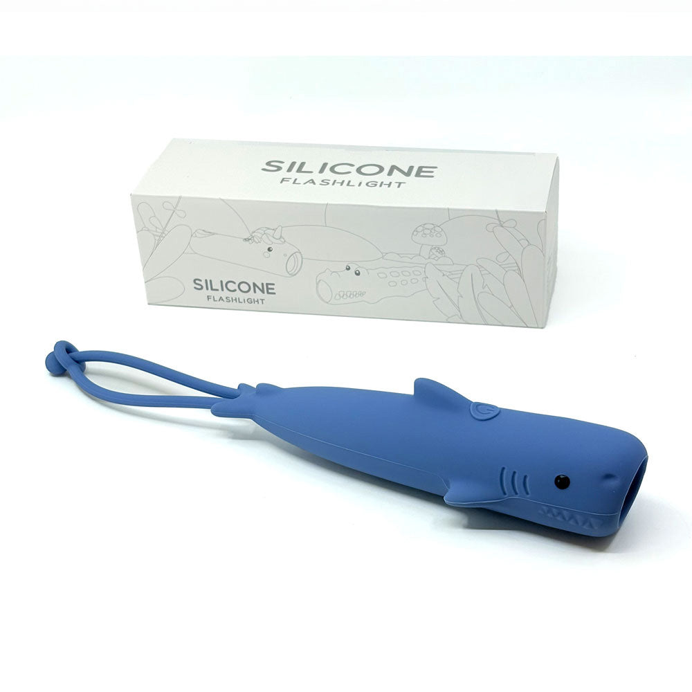 Blue silicone flashlight shaped like a shark with packaging in the background